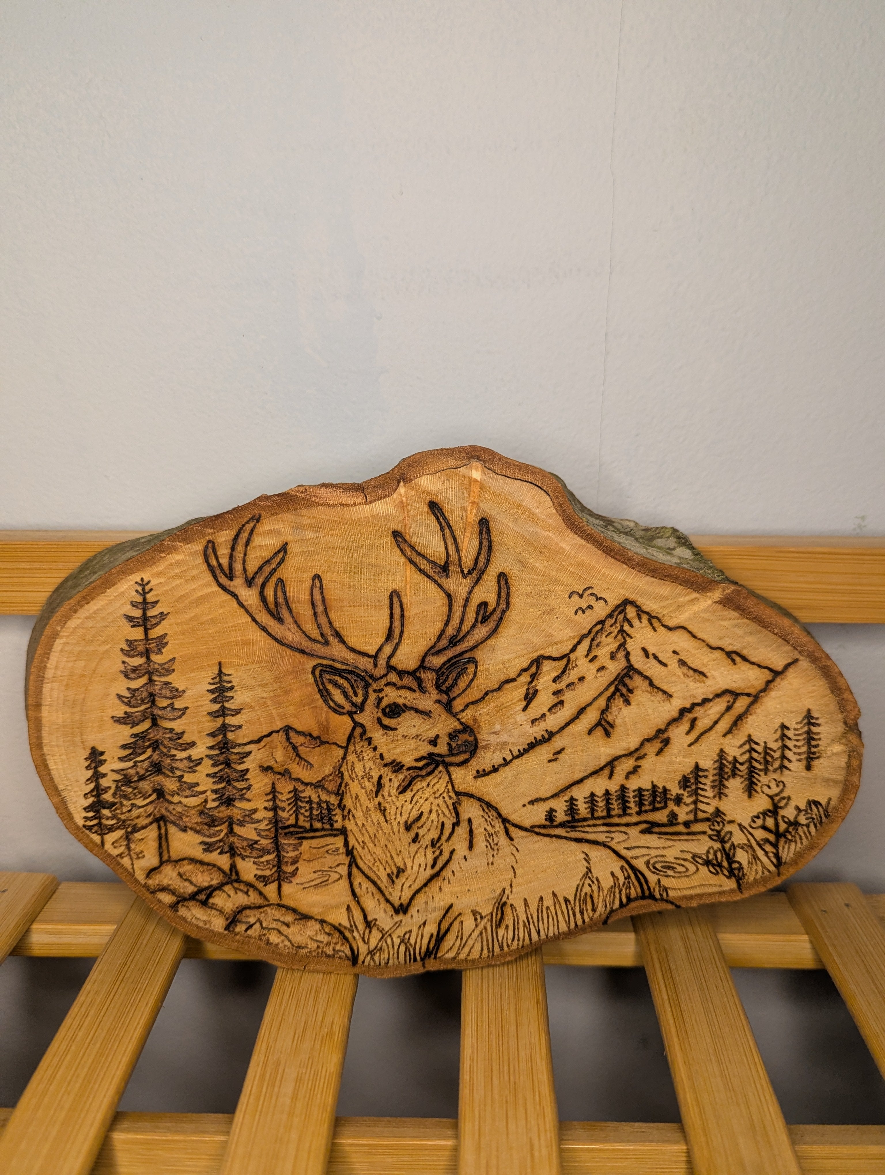 Hand-burned pyrography of a stag in a mountain landscape on a natural live-edge wood slice
